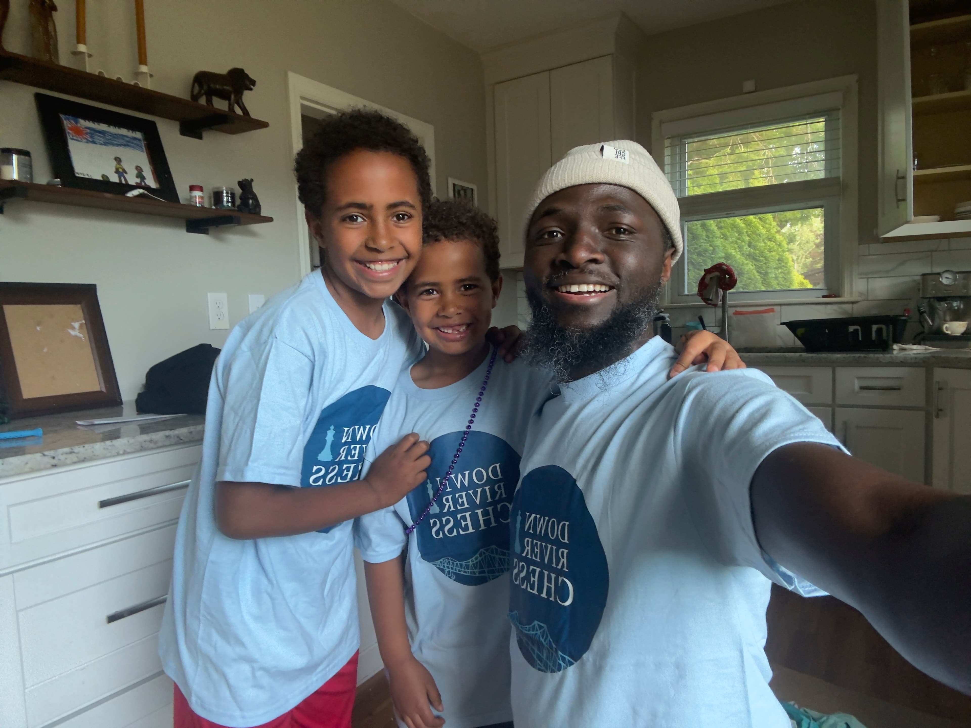 Coach Rodolfo smiling with two young chess students