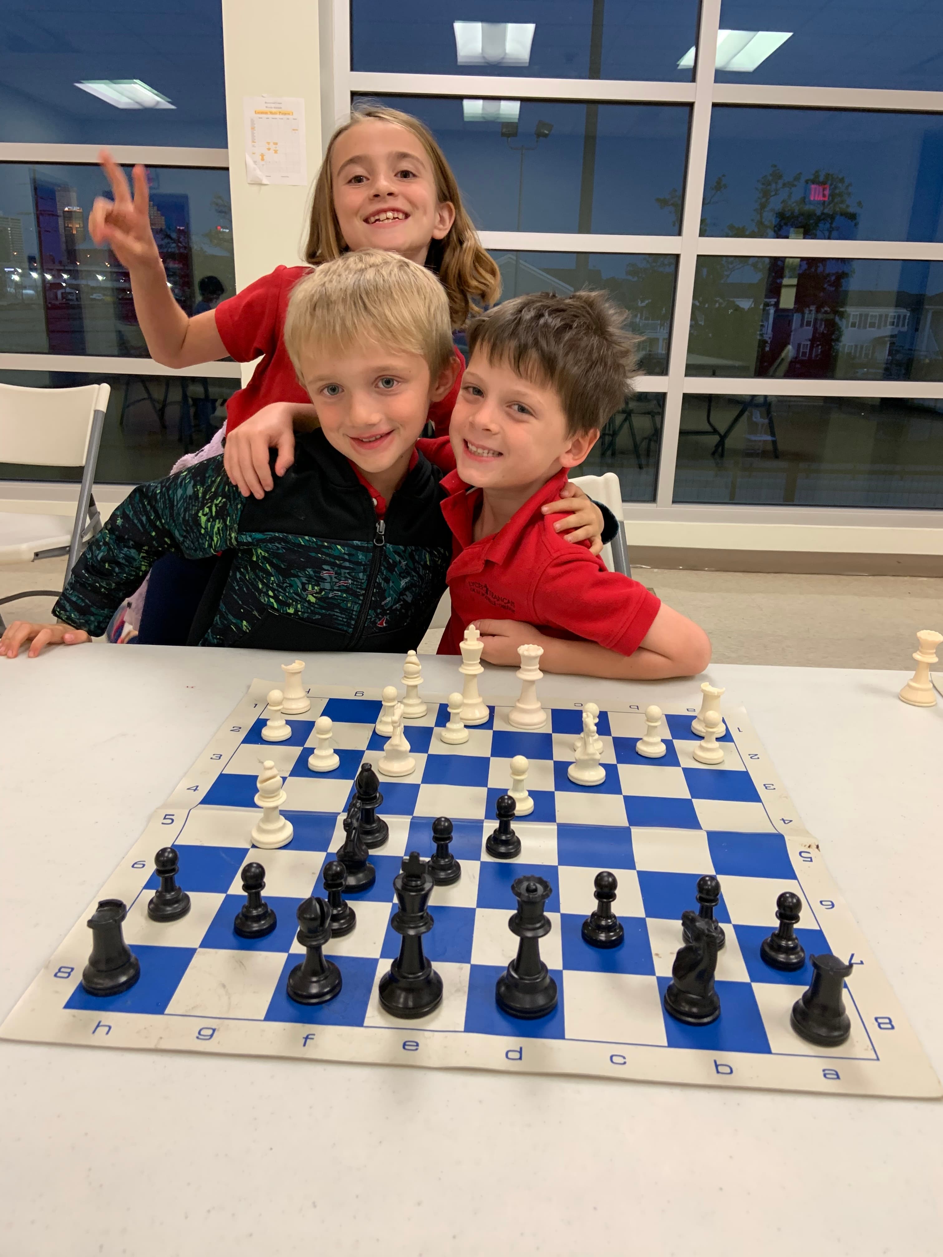 Two young chess students smiling together behind a chessboard
